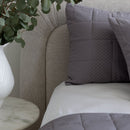 Gray textured pillows on a beige upholstered chair with a plant and vase in the background.