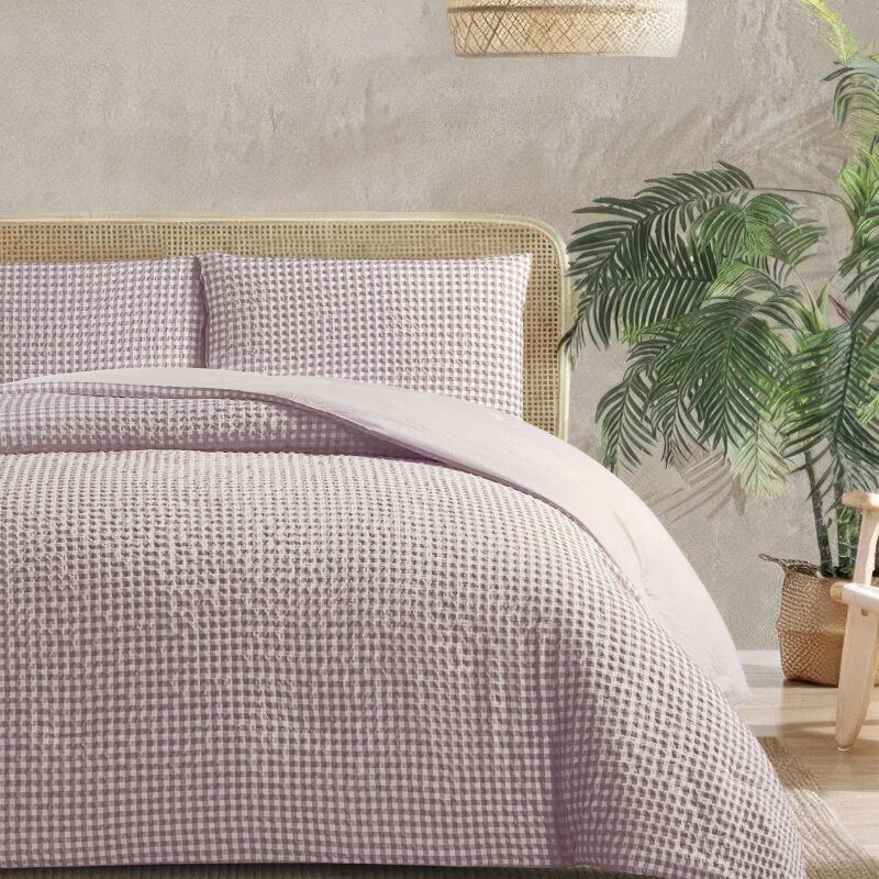 Bed with textured bedding in a bedroom setting with plants and a textured wall.