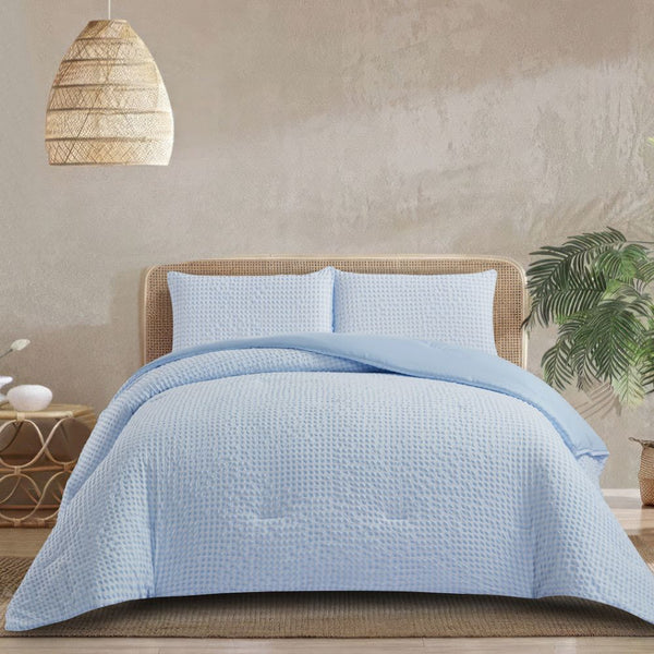Light blue quilt set on a bed with a wicker headboard and hanging lamp in a room.