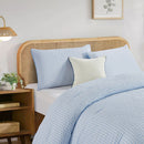 Bed with light blue bedding and pillows in a bedroom setting.