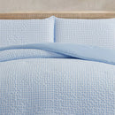Light blue textured bedding set on a bed with a beige headboard.