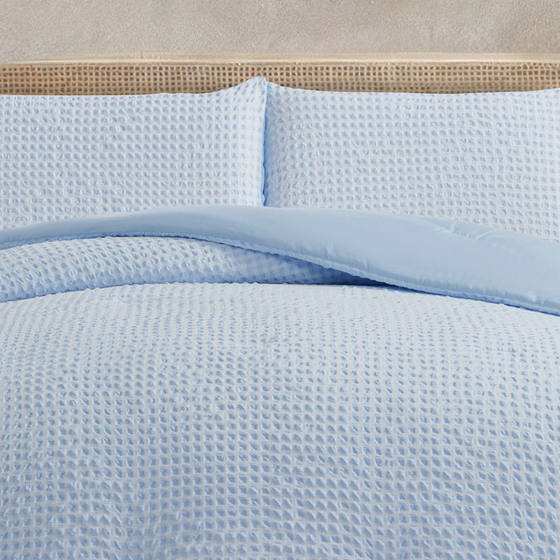 Light blue textured bedding set on a bed with a beige headboard.