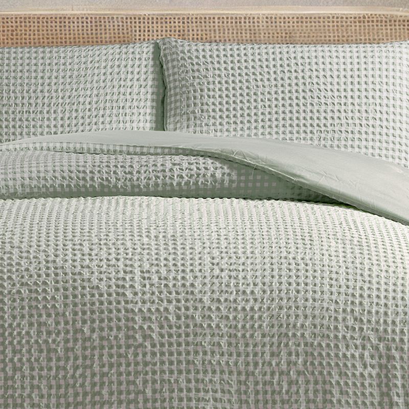 Textured green bedding set on a bed with a beige headboard.