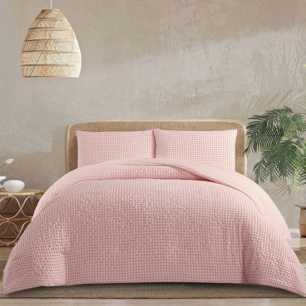 Pink quilted cover on a bed with a wicker headboard and lamp in a bedroom setting.
