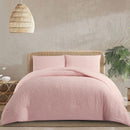 Pink quilted cover on a bed with a wicker headboard and lamp in a bedroom setting.