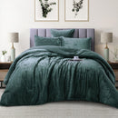 Green textured comforter set on a bed in a bedroom with lamps and wall art.
