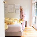 The Morgan and Reid Serene Butter Coverlet Set by Morgan and Reid, featuring a yellow coverlet and two matching pillows, brightens the room. A wooden nightstand with dried flowers and minimalist line art complete the cozy look.