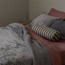 Bed with pink sheets, gray blanket, and striped pillow in a bedroom setting.