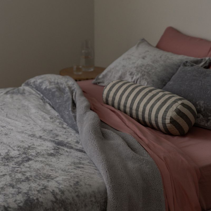 Bed with pink sheets, gray blanket, and striped pillow in a bedroom setting.