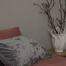 Gray pillow on a bed with a vase of branches in the background