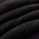 A modern bedroom features a neatly made bed with the Morgan and Reid Black Snuggle Fleece Comforter Set, accented by a white pillow, a side table with a plant and books, wall art, a pendant lamp, and sheer curtains letting in natural light.