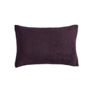 A neatly made bed with the Morgan and Reid Plum Snuggle Fleece Comforter Set and pillows sits on a light rug. Pendant lights hang above, with a side table, vase, and a large potted plant against a textured beige wall.