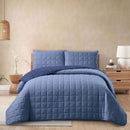 Blue quilt set on a bed in a bedroom with beige walls and wooden furniture.