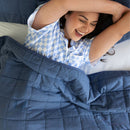 Woman under a blue weighted blanket, smiling and laughing.