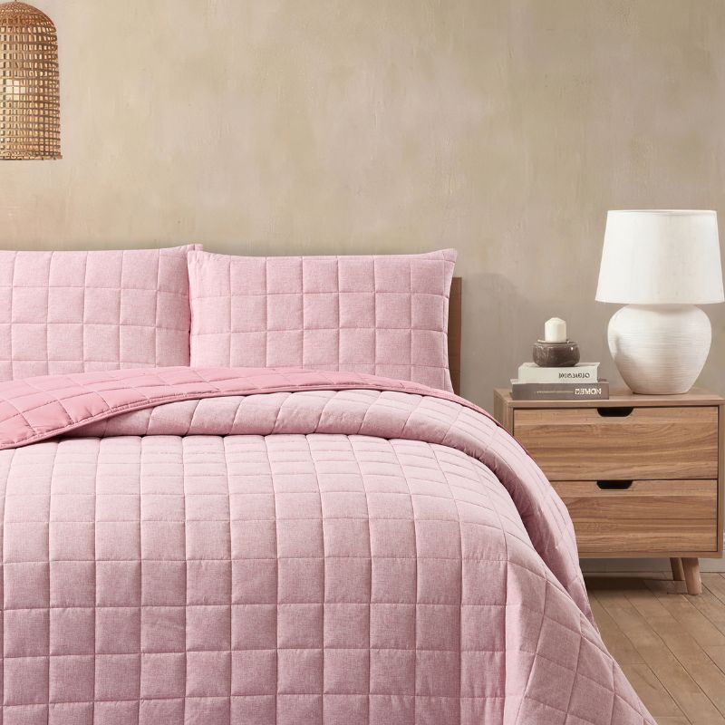 A modern bedroom displays the Morgan and Reid Hibiscus Cloudy Stitch Coverlet Set with matching pillowcases, warm toned walls, rattan pendant lighting, a wooden bedside with ceramic lamp, and a glass vase with white florals.