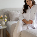 Woman in a white shirt and beige pants sitting on a couch holding a mug.