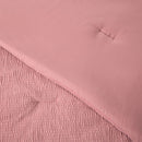 A modern bedroom features the Morgan and Reid Rose Stretch Woven Comforter Set on a neatly made bed with matching pillows, warm neutral walls, a woven pendant light, a wooden side table with a glass vase of white stems, and a ceramic lamp on a timber bedside table.