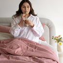Woman sitting on a couch with pink blanket, drinking from a straw