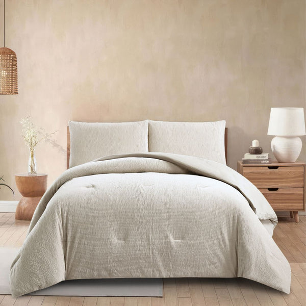 Beige comforter set on a bed in a bedroom with a lamp and plant.