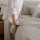 Person making a bed with beige bedding in a bedroom setting