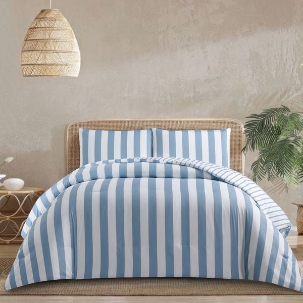 A fresh coastal bedroom features the Morgan and Reid Sea Breeze Stripe Comforter Set on a neatly styled bed with striped pillows, rattan bedhead, textured rug, natural pendant lighting, and a leafy plant beside the bed.