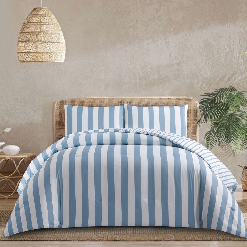 A fresh coastal bedroom features the Morgan and Reid Sea Breeze Stripe Comforter Set on a neatly styled bed with striped pillows, rattan bedhead, textured rug, natural pendant lighting, and a leafy plant beside the bed.