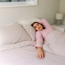 Woman in pink pajamas lying in bed with white bedding