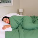 Woman sleeping under a green comforter in a bedroom setting.