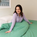 Woman sitting on a bed with green bedding in a cozy room.