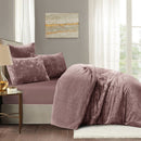 Bedroom with purple bedding and pillows, side table, and abstract painting on gray wall.