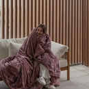 Woman wrapped in a pink blanket sitting on a couch with a wooden slat wall in the background