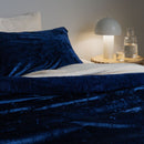 Navy blue velvet blanket on a bed with a nightstand featuring a lamp and water bottle.
