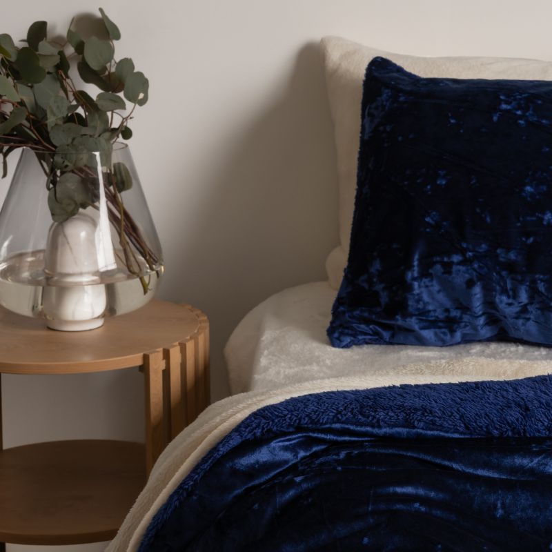 Nursery with a wooden nightstand, vase with greenery, and blue textured pillows on a bed.