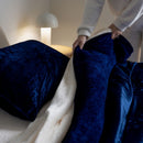 Person arranging blue and white pillows on a bed in a softly lit room.