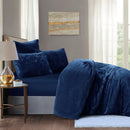 Navy blue bedding set on a bed in a bedroom with a lamp and painting.