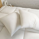 The Puradown 100% Duck Feather Cushion Insert by Puradown is displayed upright on a light wooden, ribbed cylindrical stool, set against a cream-colored textured wall and wooden floor.