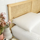 Two Puradown Hotel 100% Feather Pillows by Puradown, filled with ethically sourced Australian duck feathers, are stacked on a white quilted bed with a wooden woven headboard against a white brick wall; a vase is in the background.