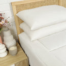 Two Puradown Hotel 100% Feather Pillows by Puradown, filled with ethically sourced Australian duck feathers, are stacked on a white quilted bed with a wooden woven headboard against a white brick wall; a vase is in the background.