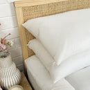 Two Puradown Hotel 100% Feather Pillows by Puradown, filled with ethically sourced Australian duck feathers, are stacked on a white quilted bed with a wooden woven headboard against a white brick wall; a vase is in the background.