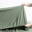 Olive organic cotton jersey pillowcase set styled on a warm-toned bed.