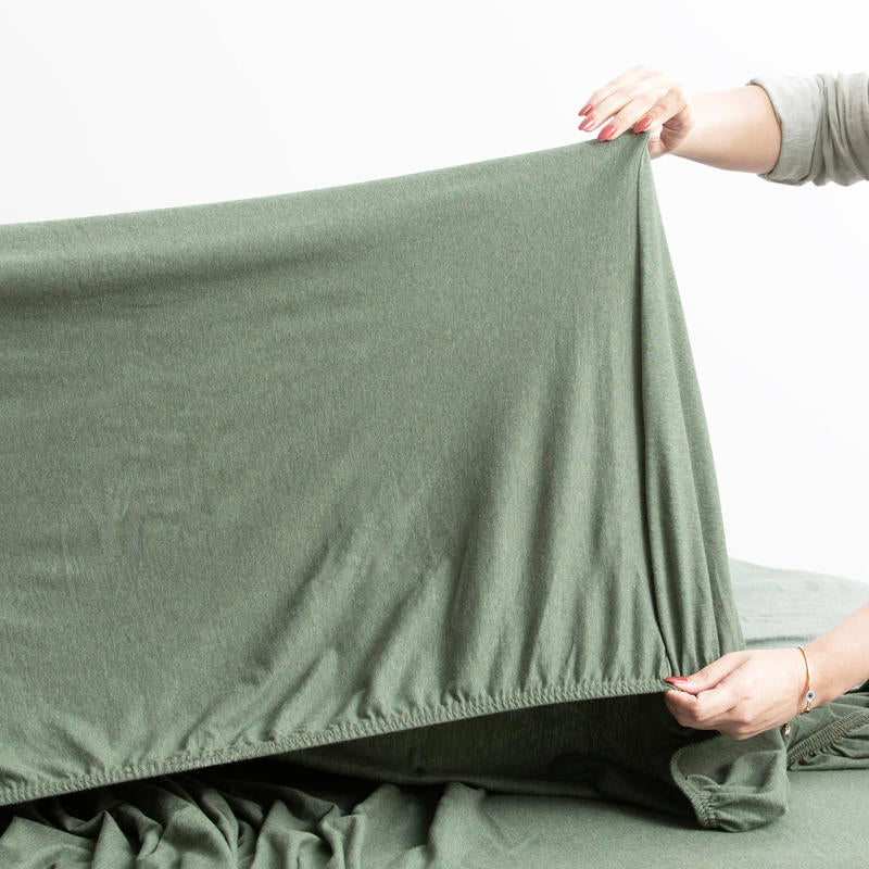 Olive organic cotton jersey pillowcase set styled on a warm-toned bed.