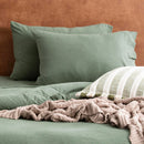 Olive organic cotton jersey pillowcase set styled on a warm-toned bed.