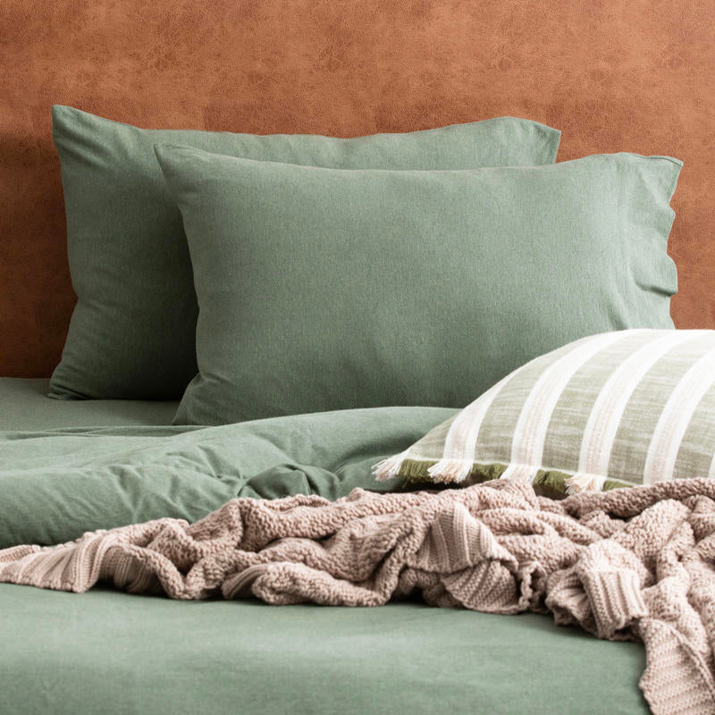 Olive organic cotton jersey pillowcase set styled on a warm-toned bed.