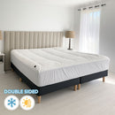 A modern bedroom features a light upholstered headboard, Sienna Living Luxury Hotel 1500GSM Reversible Mattress Topper, black bed base with wooden legs, a bedside table and lamp, with sunlight streaming through sheer curtains.