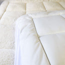 A modern bedroom features a light upholstered headboard, Sienna Living Luxury Hotel 1500GSM Reversible Mattress Topper, black bed base with wooden legs, a bedside table and lamp, with sunlight streaming through sheer curtains.