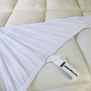 A modern bedroom features a light upholstered headboard, Sienna Living Luxury Hotel 1500GSM Reversible Mattress Topper, black bed base with wooden legs, a bedside table and lamp, with sunlight streaming through sheer curtains.