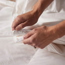 A neatly made bed with the Sienna Living Luxury 4 Seasons Duck Feather Down 2-in-1 Quilt and two pillows, set against a large rounded beige headboard, blue wall, and brown floor.