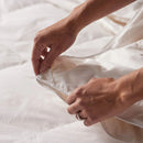 A neatly made bed features the Sienna Living Luxury 4 Seasons Goose Feather Down 2-in-1 Quilt by Sienna Living for year-round comfort. Two pillows rest against a curved beige headboard and blue wall above a light brown floor.