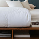 A neatly made bed features the Sienna Living All Seasons Hungarian Goose Down Quilt and white pillows against a dark blue paneled wall. A wooden bench at the foot of the bed adds all-season versatility to this clean, modern look.