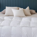 A neatly made bed features the Sienna Living All Seasons Hungarian Goose Down Quilt and white pillows against a dark blue paneled wall. A wooden bench at the foot of the bed adds all-season versatility to this clean, modern look.